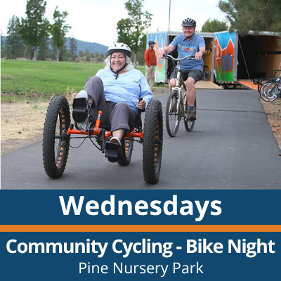 Wednesdays. Community Cycling Bike Night. Pine Nursery Park. A person smiles while riding a three-wheeled bicycle on a paved path, with another person riding a bike behind them and a trailer and trees visible in the background.