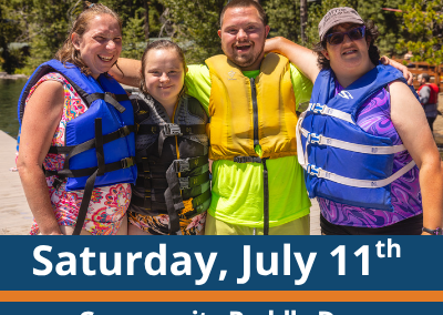 Saturday, July 11th. Community Paddle Day. Camp Tamarack. Four people stand close together outdoors near the water, wearing life jackets and smiling with their arms around each other, with trees and shoreline in the background.