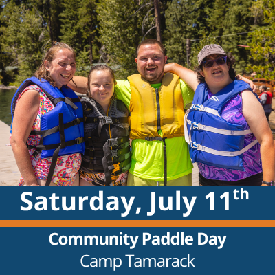Saturday, July 11th. Community Paddle Day. Camp Tamarack. Four people stand close together outdoors near the water, wearing life jackets and smiling with their arms around each other, with trees and shoreline in the background.