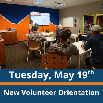 Classroom scene; a group of adults sit at tables facing a presenter standing near a screen at the front of the room; the presenter gestures toward the screen while speaking; text at the bottom reads “Tuesday, May 19th” and “New Volunteer Orientation.”