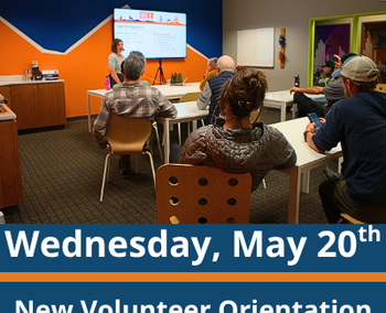 Classroom scene; a group of adults sit at tables facing a presenter standing near a screen at the front of the room; the presenter gestures toward the screen while speaking; text at the bottom reads “Wednesday, May 20th” and “New Volunteer Orientation.”