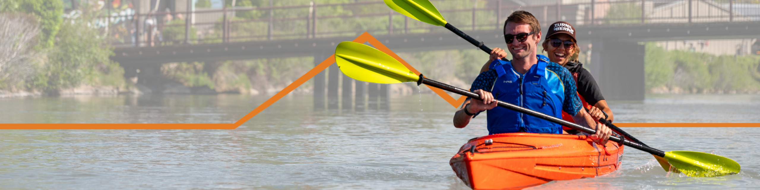 Two people paddle an orange tandem kayak across calm water. Both wear PFDs and use bright yellow paddles while a bridge spans the river behind them. An orange mountain shaped graphic overlays the image.