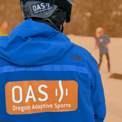 a person wearing a blue north face ski jacket with the orange O-A-S logo 
