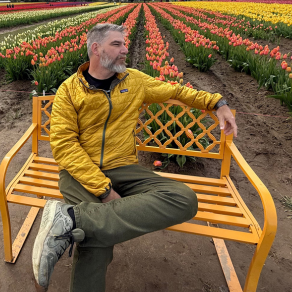 Jared, a man with silver hair and a beard, sits on a yellow bench in front of rows of tulips