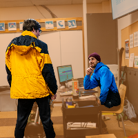 two men talk over a desk with a computer and other technology on it in the OAS room at Mt. Bachelor